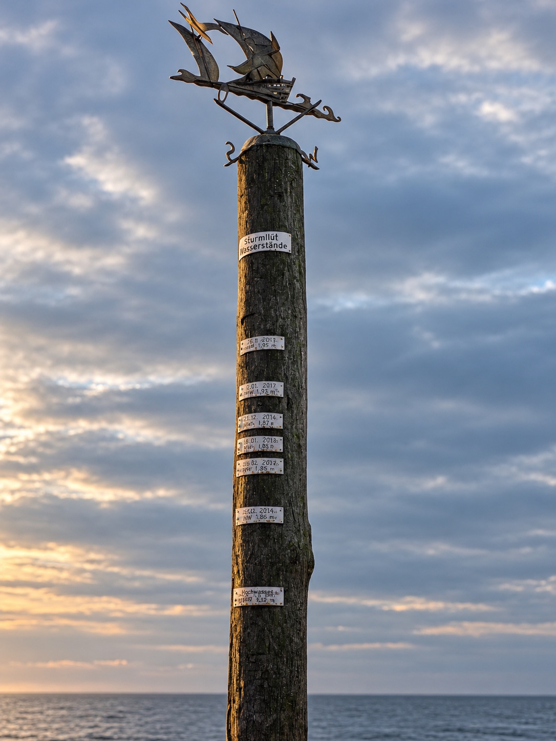 Sturmflutpfahl mit Schiffswindfahne am Meer